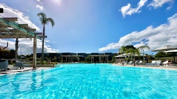 Une piscine d’eau cristalline, bordée de chaises longues et d’ombrelles, entourée de palmiers et de bâtiments.