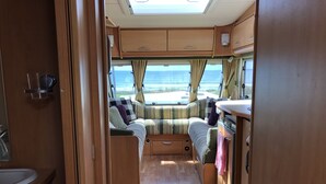 Un intérieur de camping-car compact comprenant un coin cuisine, un espace repas et un coin nuit avec vue sur l’océan.