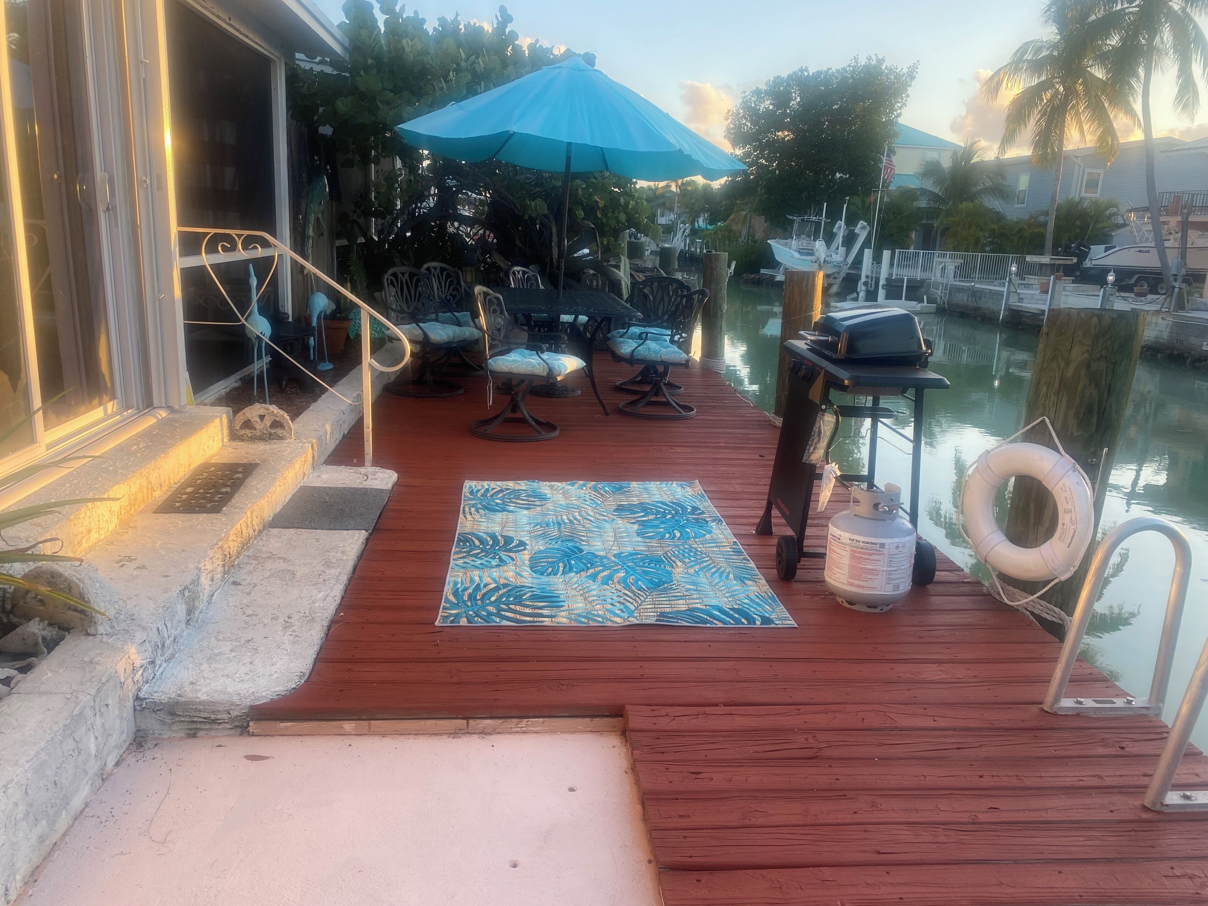 A wooden deck with outdoor seating, a blue umbrella, and a waterway view.