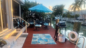 A wooden deck with outdoor seating, a blue umbrella, and a waterway view.