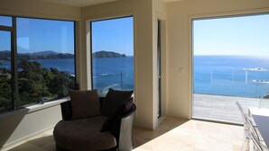A spacious room with large windows offering a view of the sea and distant hills. - Stunning Views on the Coast (Taupiri Bay)