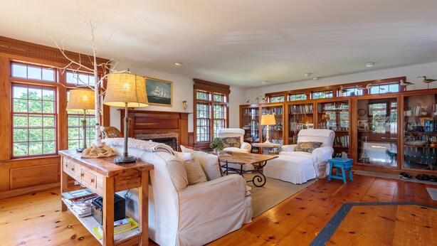 A spacious living room with wooden floors, a fireplace, a large bookshelf, and a cozy seating area. - Nantucket Private Oasis - 6BR Pet-Friendly Home, Short Drive to Quidnet Beach (Nantucket)