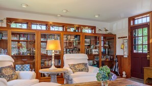 A cozy reading room with a fireplace, comfortable seating, and a large wooden bookshelf filled with books. - Nantucket Private Oasis - 6BR Pet-Friendly Home, Short Drive to Quidnet Beach (Nantucket)
