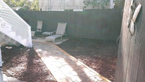 Ein Garten mit einem gepflasterten Weg, der zu zwei weißen Stühlen, einem Holzzaun und einer Metallkonstruktion führt.