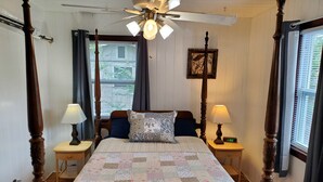Ein Bett mit Baldachin, eine Bettdecke, zwei Nachttischlampen, ein Deckenventilator und ein Fenster mit Jalousien.