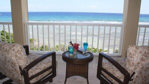 Un balcón con mobiliario de mimbre y una mesa de vidrio, con vista a una playa y el océano.