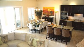 Amplia sala de estar con un sofá en forma de L, una mesa de comedor con sillas y una cocina con armarios oscuros y microondas.