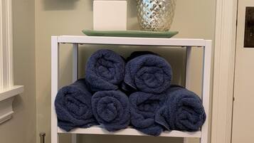 Een witte plank met netjes gevouwen donkerblauwe handdoeken, een decoratieve glazen vaas en een witte zeephouder.