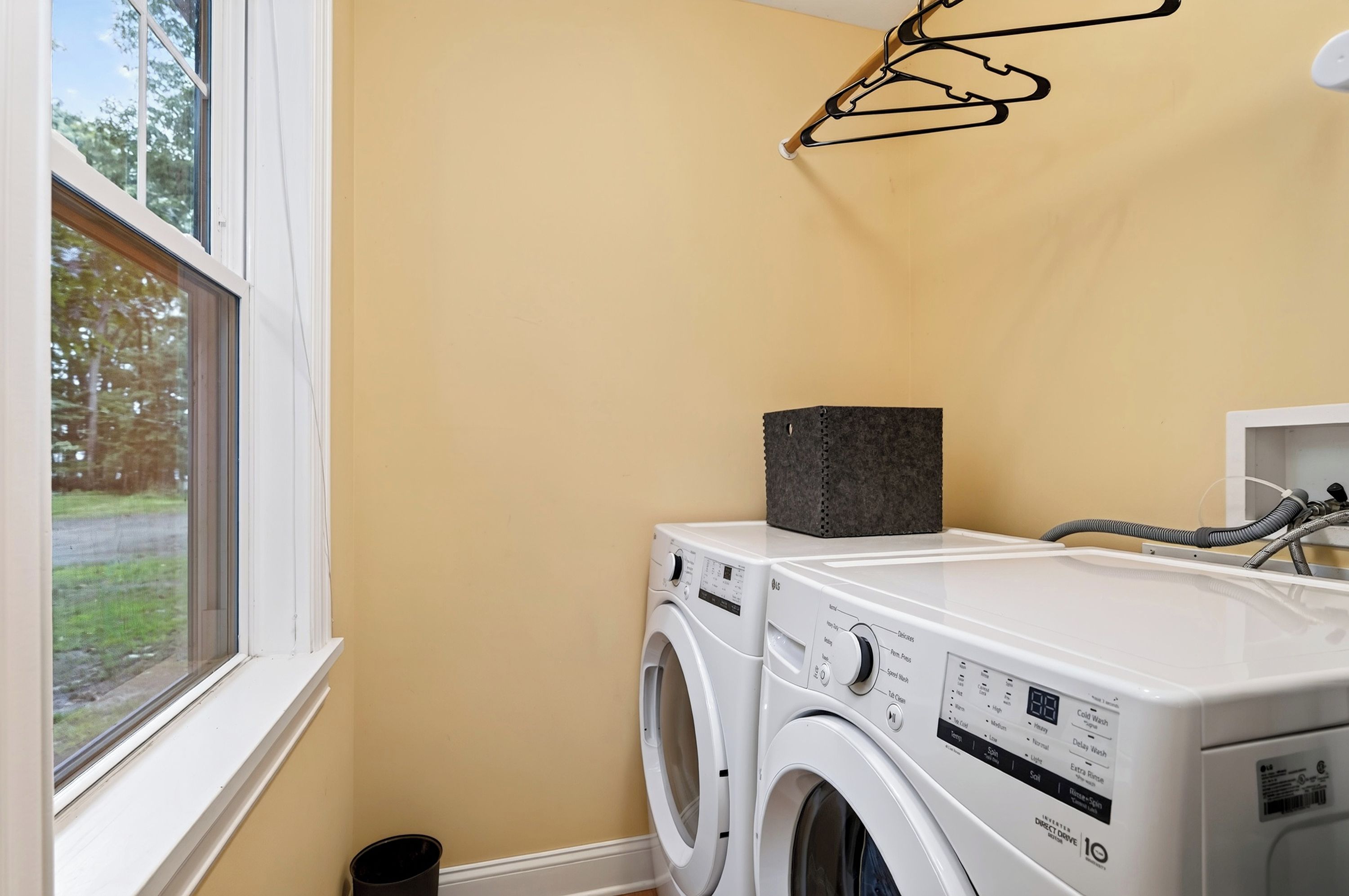 A laundry room with two washing machines, a drying rack, and a window.