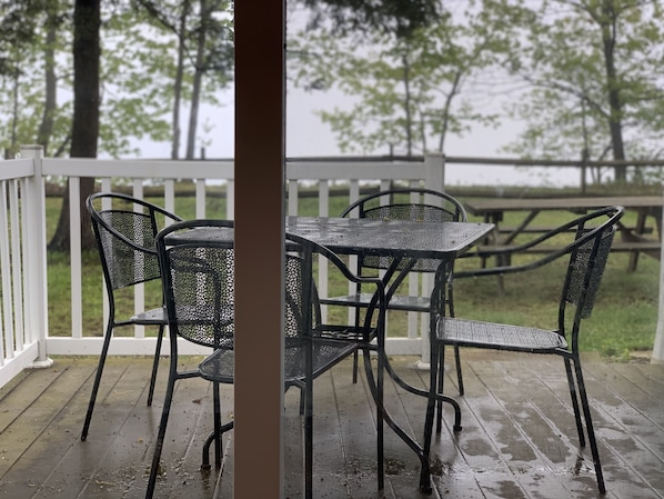 Un espacio de estar al aire libre techado, con barandilla blanca, sillas de metal y una mesa.