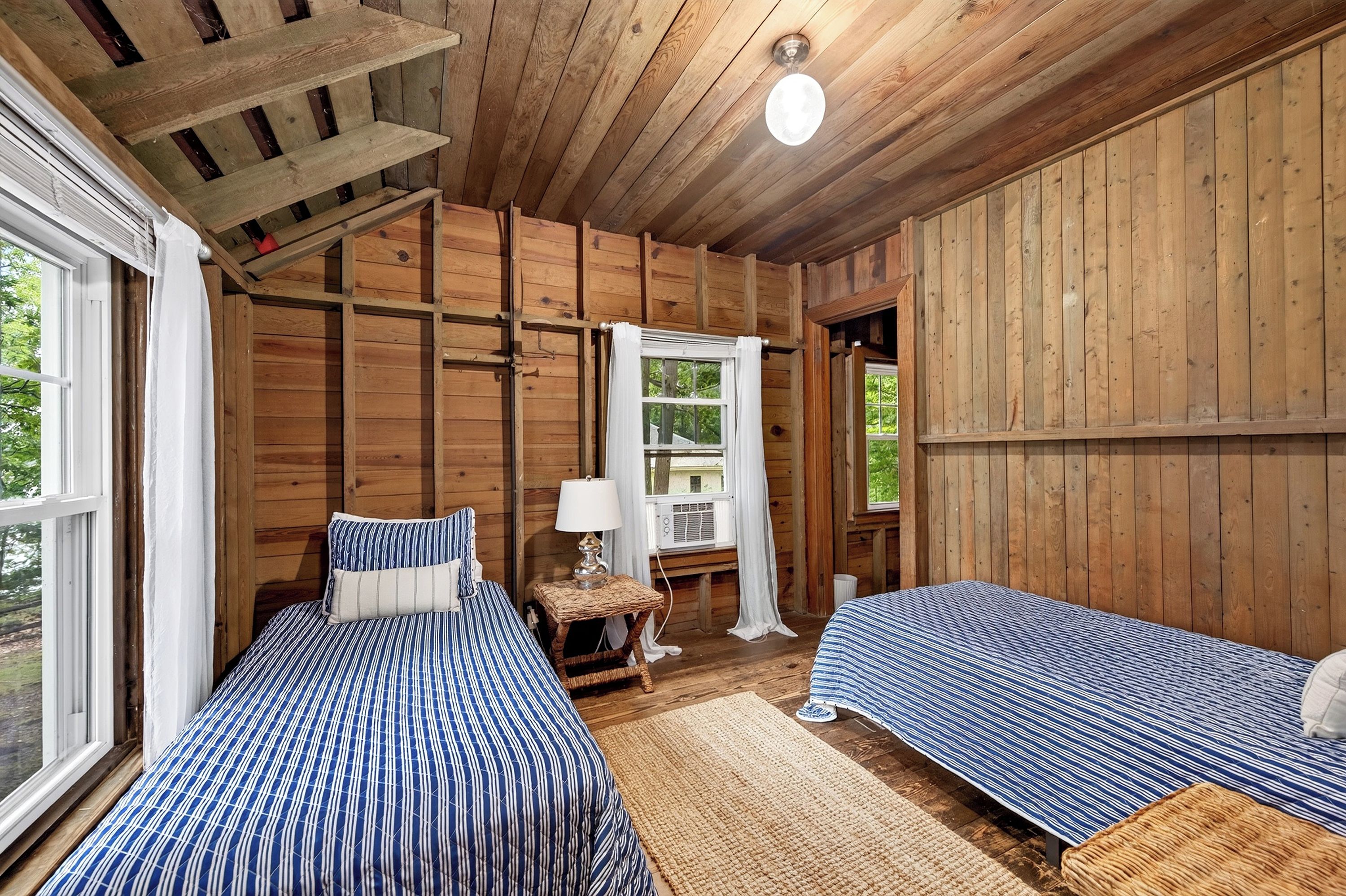 A wooden cabin bedroom with two beds, a window, and a ceiling fan.