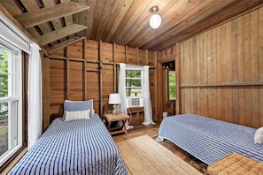 Un dormitorio de cabaña de madera con dos camas, una ventana y un ventilador de techo.