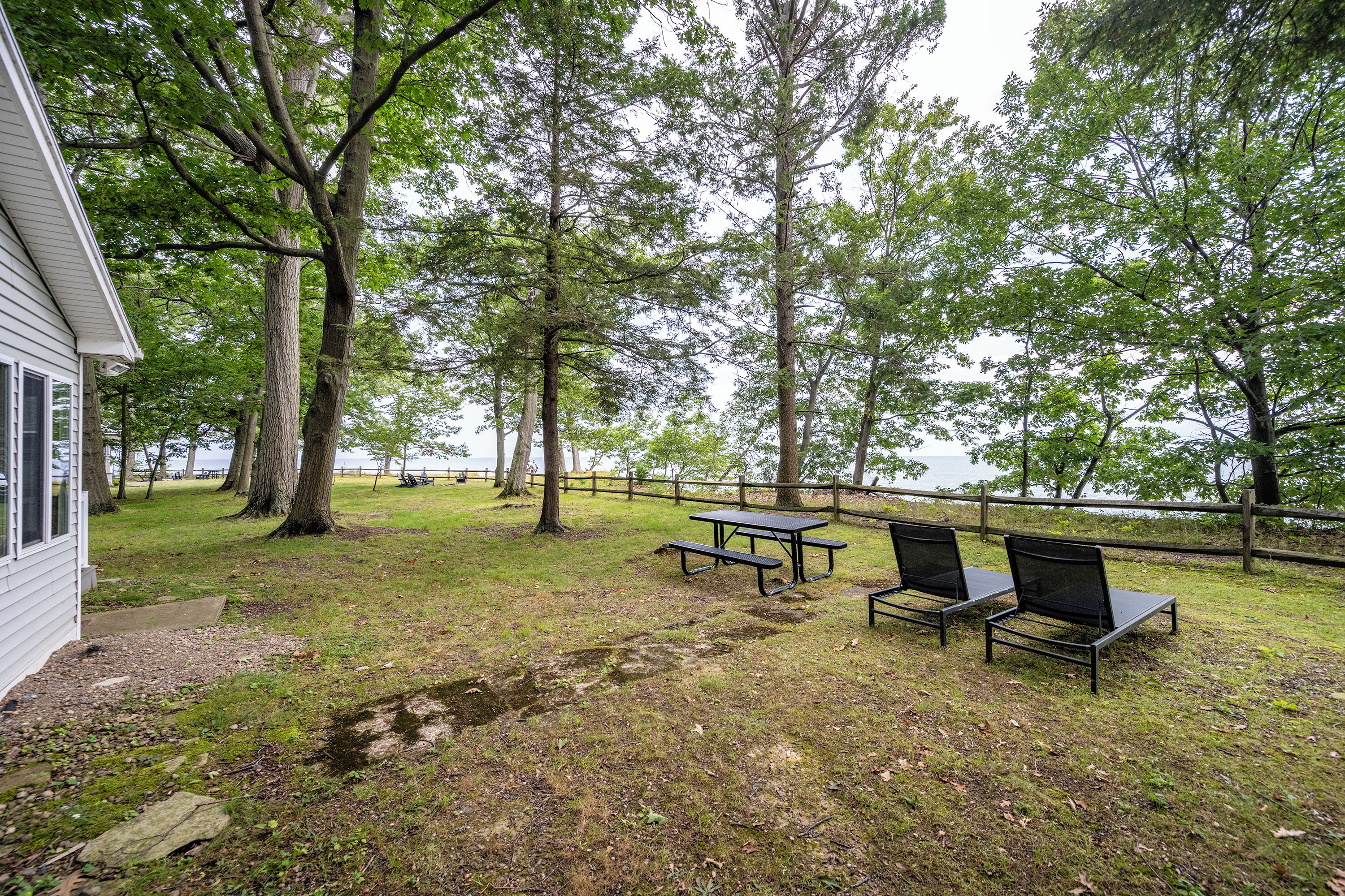 Un espace extérieur verdoyant avec des tables et des chaises de pique-nique, une clôture en bois et un bâtiment en arrière-plan.