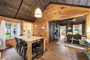 A wooden interior with a dining area, a sofa, and a kitchen visible through an open door. - "The Richard" 3BR Lakefront: 60-Ac Estate Access with Private Beach sleeps 8 (Irving)