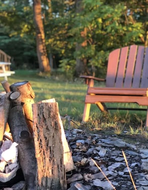 A wooden fire pit with logs and a chair in a wooded area. - "The Richard" 3BR Lakefront: 60-Ac Estate Access with Private Beach sleeps 8 (Irving)
