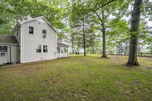 A two-story house with a porch, surrounded by a grassy yard and tall trees.