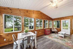 A cabin with large windows, a dining area, and a ceiling fan. - "The Richard" 3BR Lakefront: 60-Ac Estate Access with Private Beach sleeps 8 (Irving)
