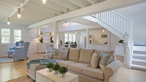 A spacious living area with a high ceiling, a large sofa, a coffee table, and a staircase leading to an upper level. - The Cottage North Narooma (NORTH NAROOMA)