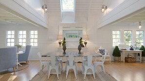 A dining area with a white table, white chairs, and a central chandelier. - The Cottage North Narooma (NORTH NAROOMA)