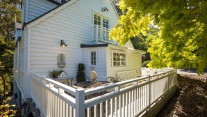 A white house with a fenced porch, a small attached structure, and a garden area. - The Cottage North Narooma (NORTH NAROOMA)