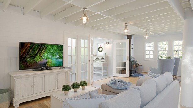 A spacious living room with a large flat-screen TV, white furniture, and a fireplace. - The Cottage North Narooma (NORTH NAROOMA)
