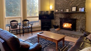 A living room with a stone fireplace, a television, and two chairs.