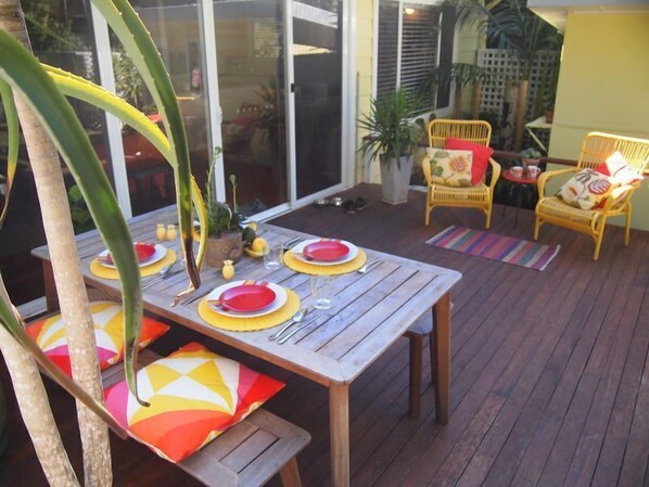 Een terras buiten met een houten eettafel, omringd door rieten stoelen en een potplant.