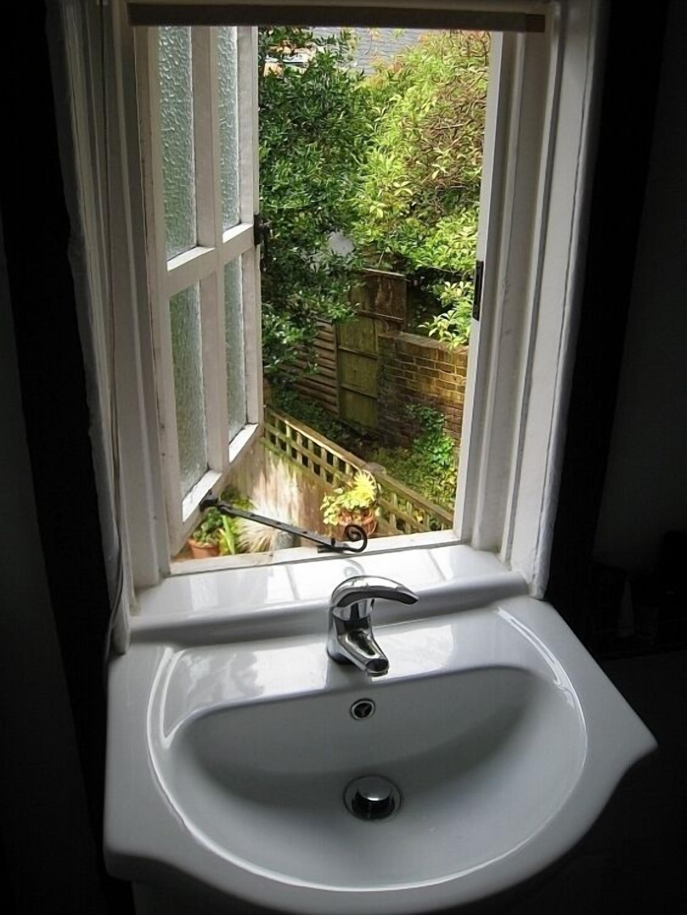 Un lavamanos de baño con una ventana que da a un jardín con valla de madera y plantas en macetas.