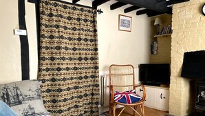 Een gezellige woonkamer met een kamerkleed, een rieten stoel met een kussen met Union Jack print, een bank met decoratieve kussens en een open haard.