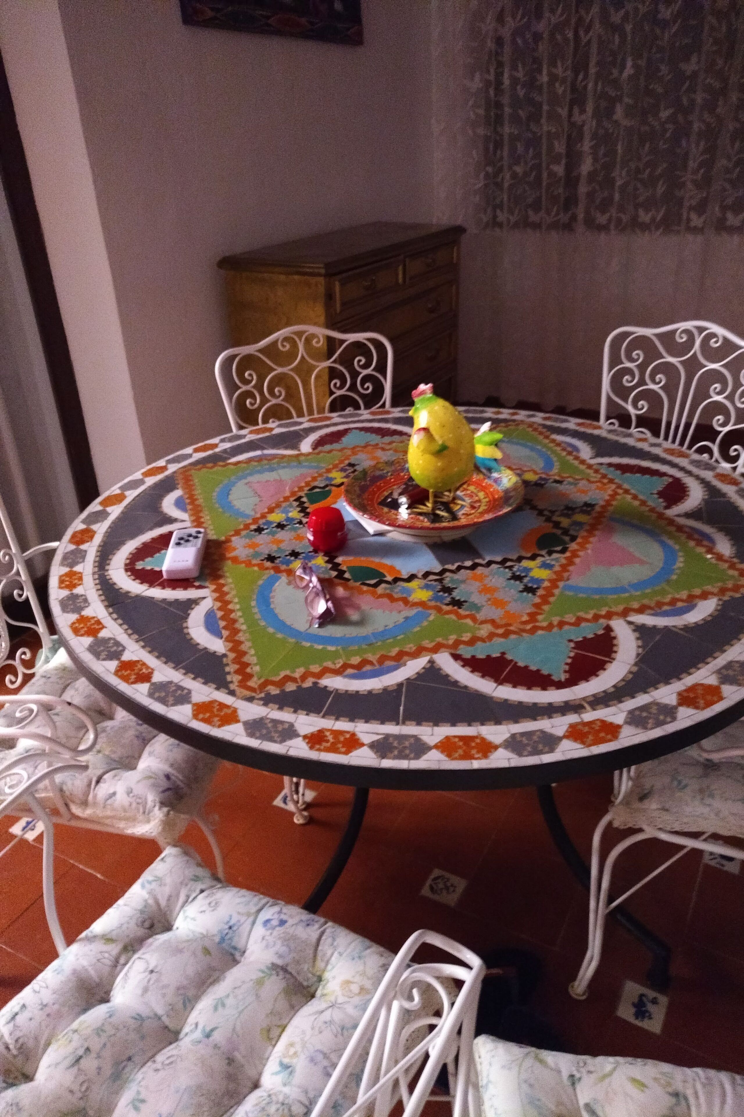 A round table with a colorful tablecloth, surrounded by white chairs with floral upholstery.