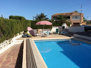 A swimming pool with lounge chairs and umbrellas, a stone wall, and a building with a tiled roof in the background. - 5 DBR villa.Dual level with own pool. Walking distance to Calpe's Levante beach (Alicante)