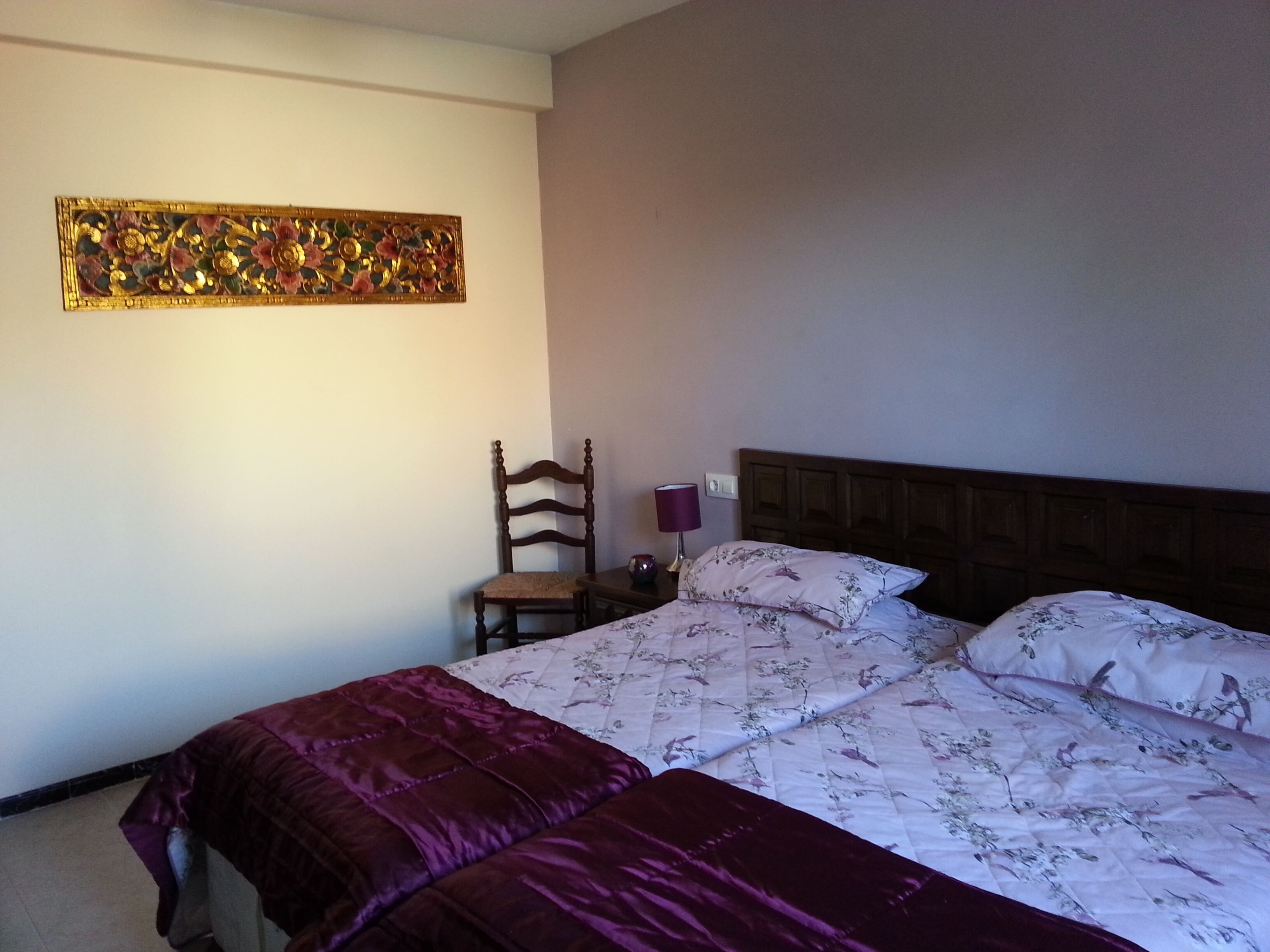 A bedroom with a bed, a chair, a nightstand, and a wall decoration.