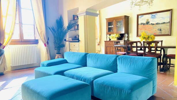 A living room with a blue sectional sofa, a dining table with chairs, a potted plant, and a painting on the wall. - || NEW Incredible View || Piazza della Signoria apt! (Firenze)