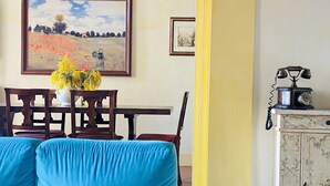 A living room with a blue sofa, a dining table with chairs, a chandelier, a painting, a telephone, and a cabinet. - || NEW Incredible View || Piazza della Signoria apt! (Firenze)