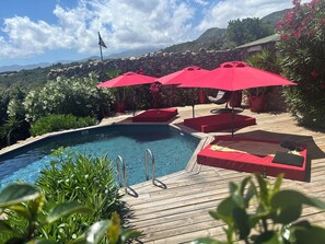 A pool area with red umbrellas, wooden deck, and stone wall.