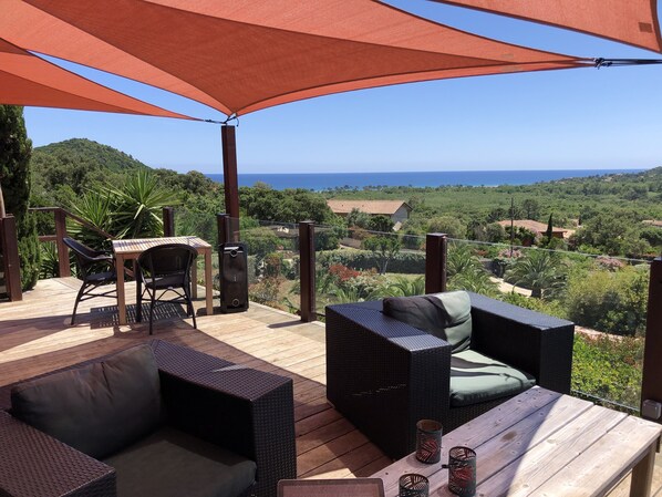 A wooden deck with wicker furniture, a table, and a large umbrella providing shade.