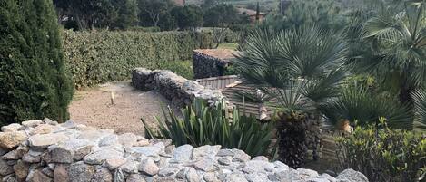 Un mur de pierres bordé d’un chemin de gravier menant à un bâtiment rustique surmonté d’un toit en tuiles.