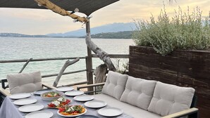 Un espace de restauration en plein air avec une table dressée pour deux personnes, offrant une vue sur un plan d’eau et des montagnes.