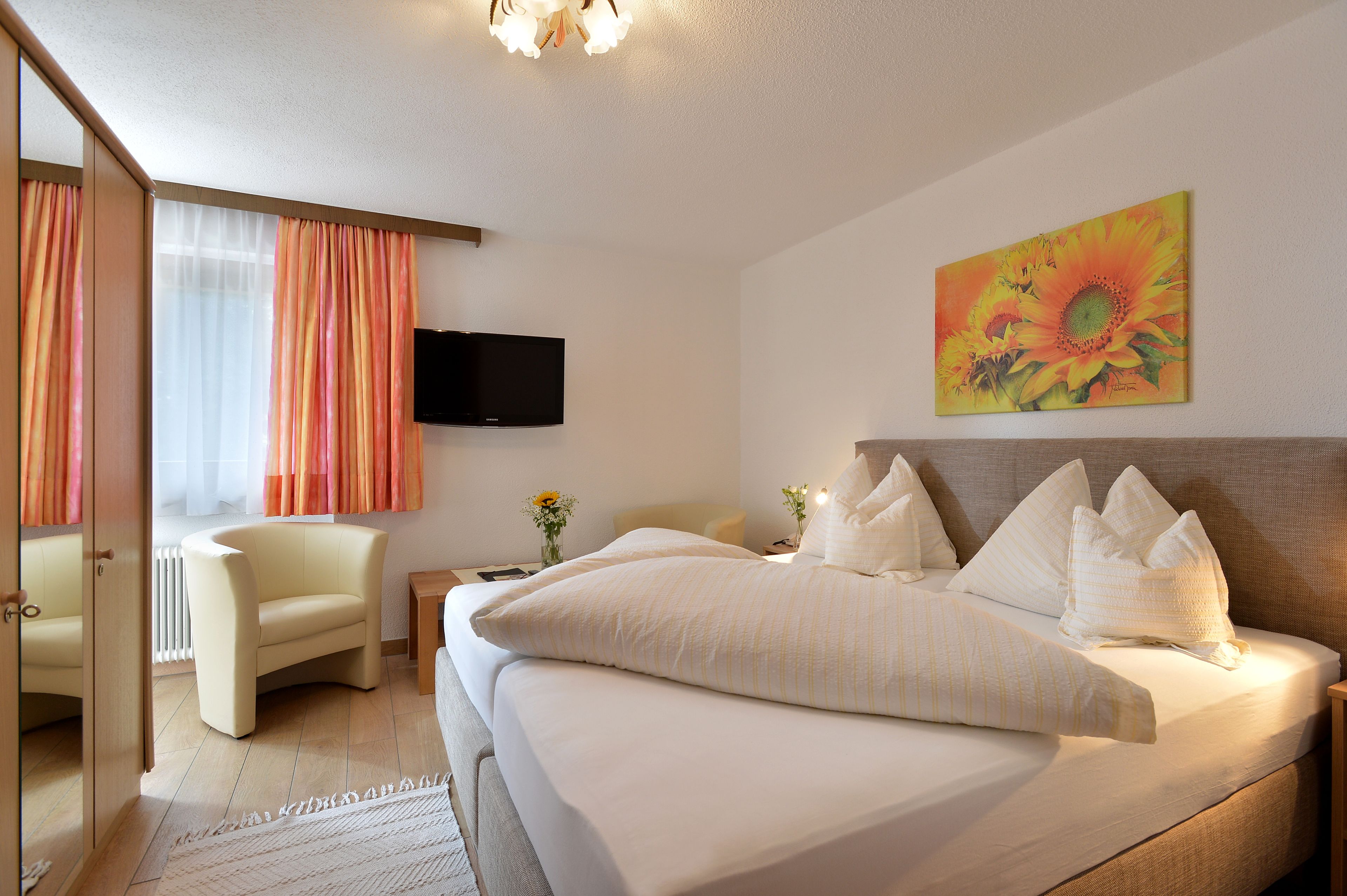A hotel room with a bed, a chair, a TV, and a painting.