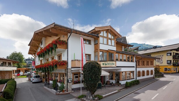 A hotel with a balcony adorned with red flowers, a sign reading "Hotel Gais Theresein," and a mountain backdrop. - Hotel Theresia Garni (Sankt Johann in Tirol)