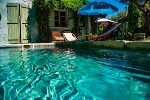 A clear pool with a wooden deck, lounge chairs, and a hammock.