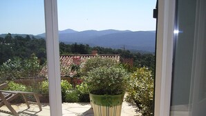 A view from a room with a sliding glass door leading to an outdoor patio with a potted plant, a chair, and a tiled floor. - Hillside Village House with Stunning Views toward St Tropez (La Garde-Freinet)
