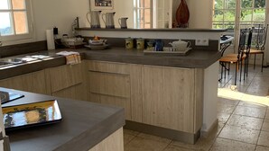 A spacious kitchen with a large island, wooden cabinets, and a view of the garden through the windows. - Hillside Village House with Stunning Views toward St Tropez (La Garde-Freinet)