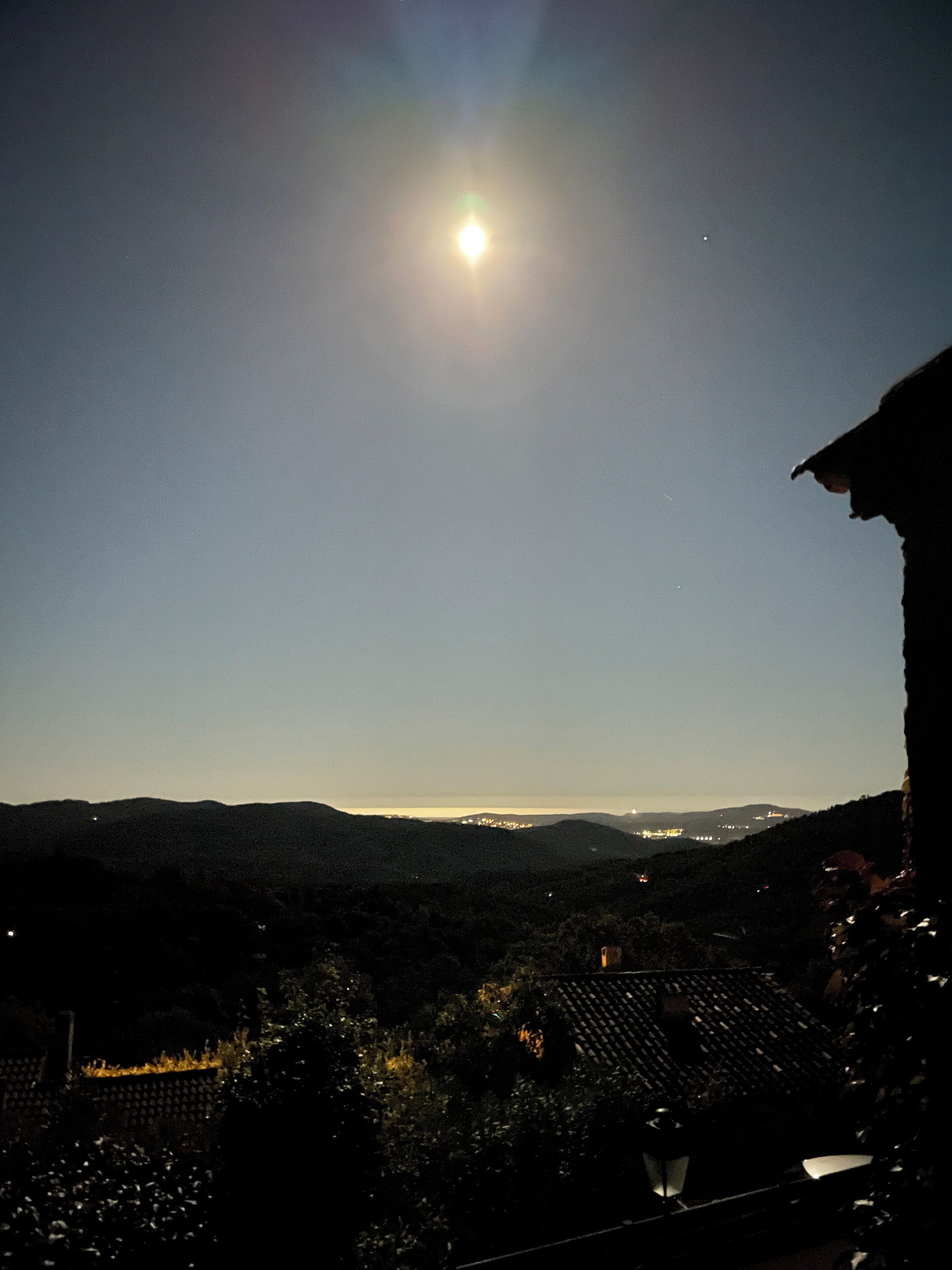 A night view of a mountainous landscape with a bright moon and distant city lights.