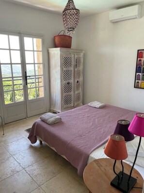 Un dormitorio con cama, armario, candelabro, aire acondicionado y ventana con vistas.