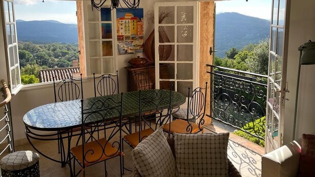 A dining area with a table and chairs, a bookshelf, and a view of the mountains. - Hillside Village House with Stunning Views toward St Tropez (La Garde-Freinet)