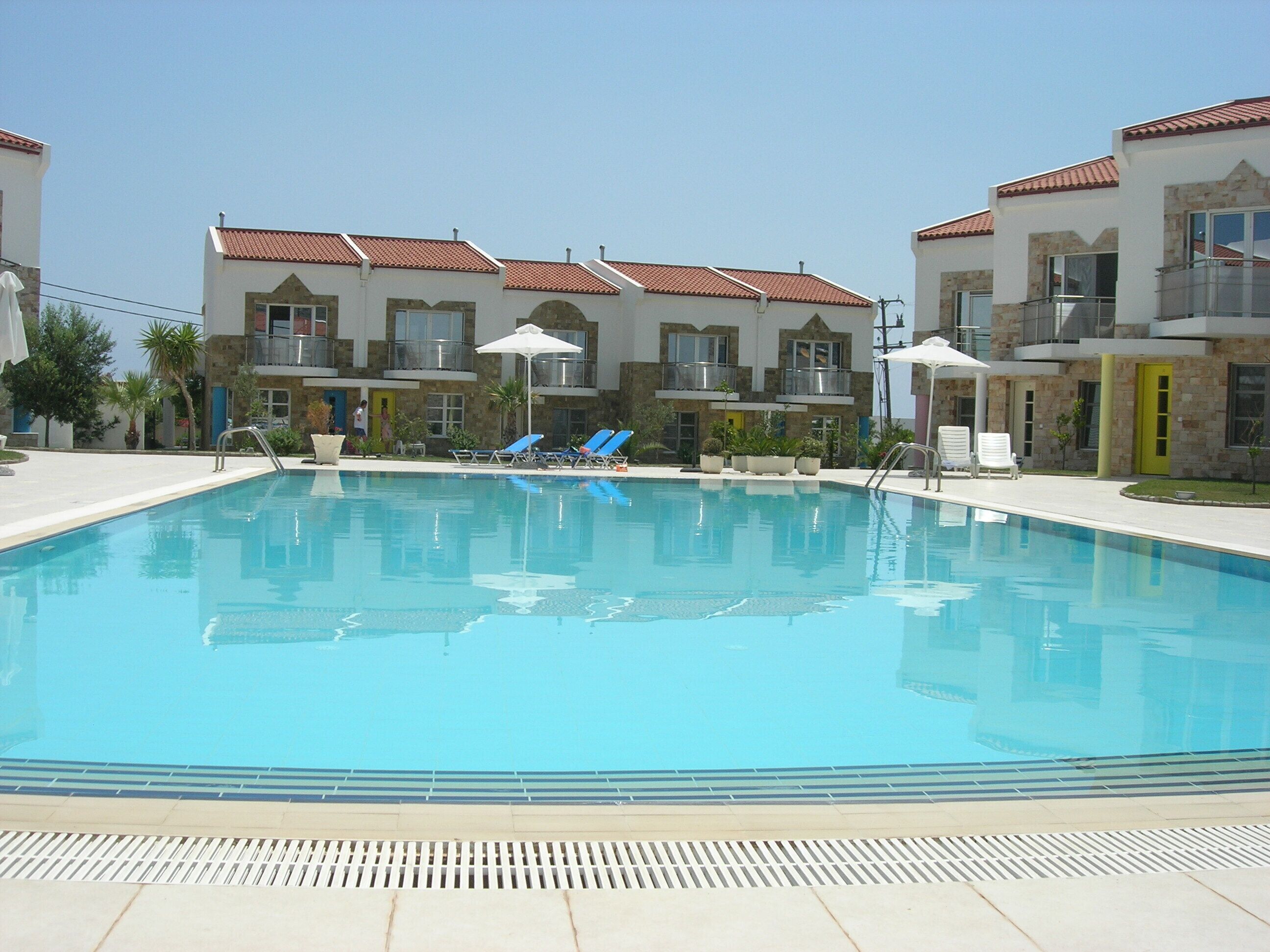 A swimming pool with lounge chairs and umbrellas, surrounded by multi-story buildings with balconies and windows.