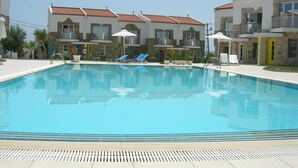 A swimming pool with lounge chairs and umbrellas, surrounded by multi-story buildings with balconies and windows. - Seaview Villa. Quiet and peaceful, relax and chill out (Lassithi)