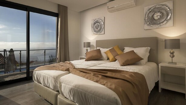 A modern bedroom with a large bed, two bedside tables, and a view of the city through floor-to-ceiling windows. - Villa Guinea - Fantastic House With Spectacular Views And Pool  (Funchal- Madeira)