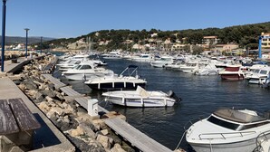 Un port de plaisance où sont amarrés de nombreux bateaux, une côte rocheuse et, en arrière-plan, des bâtiments et des collines.